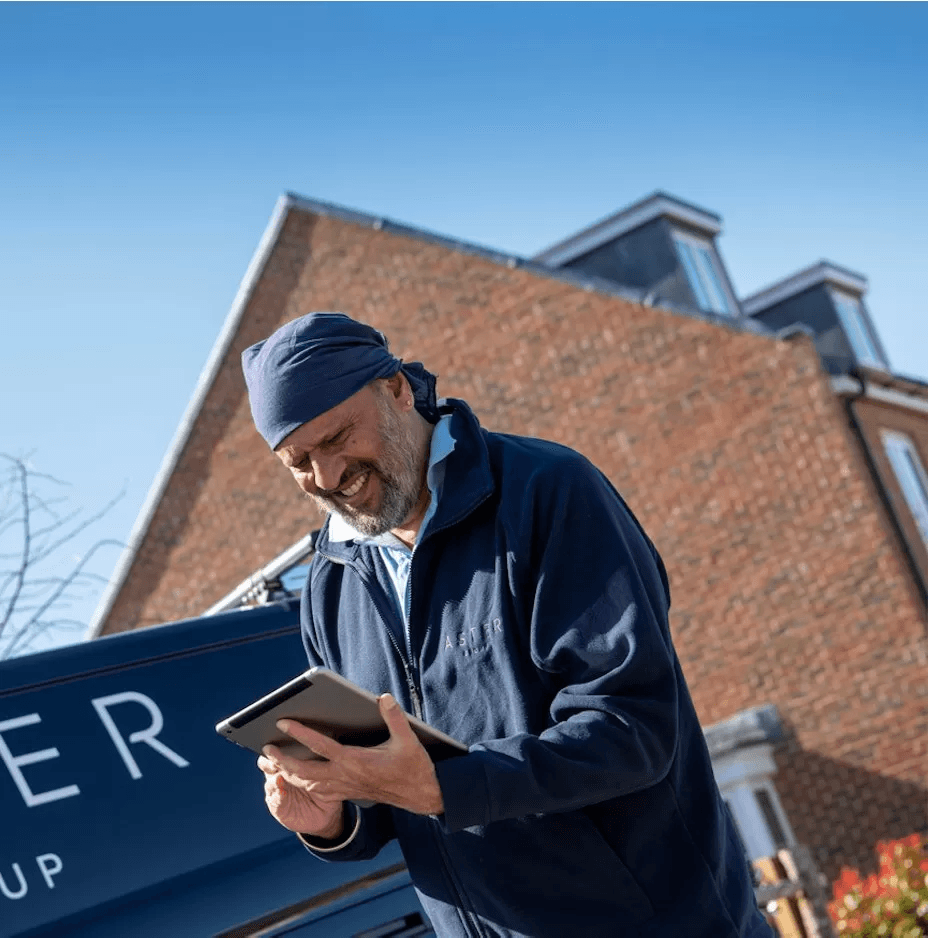 Image of a man smiling , he is holding a tablet device in his hand which he is looking at.