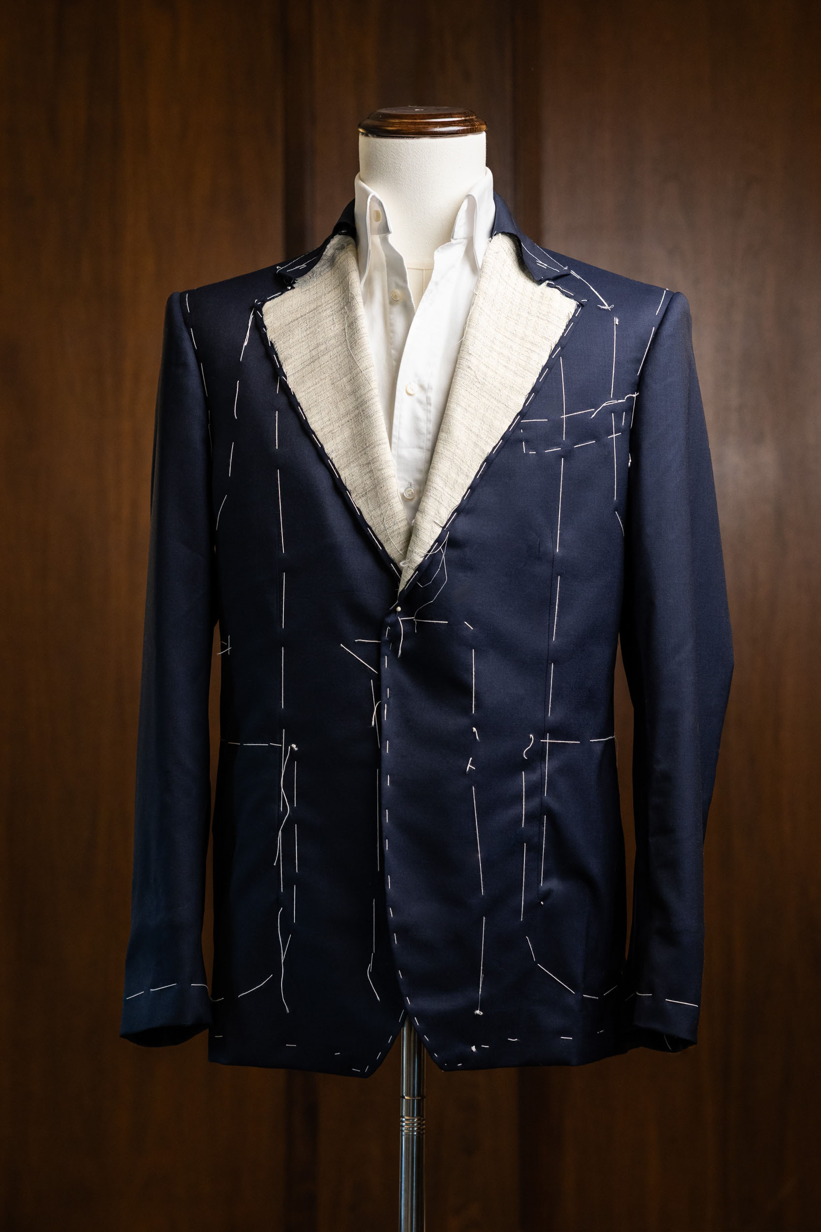 A handcrafted Don Marrón bespoke navy jacket in its basted fitting stage, showcasing hand-stitched canvas, exposed construction lines, and artisanal tailoring details.”