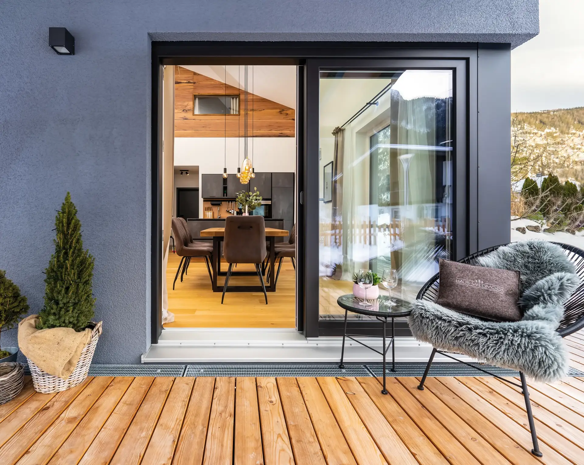 Modernes Wohnzimmer mit Essbereich, zugänglich durch eine Schiebetür, und eine gemütliche Sitzecke im Freien mit Blick auf eine bergige Landschaft.