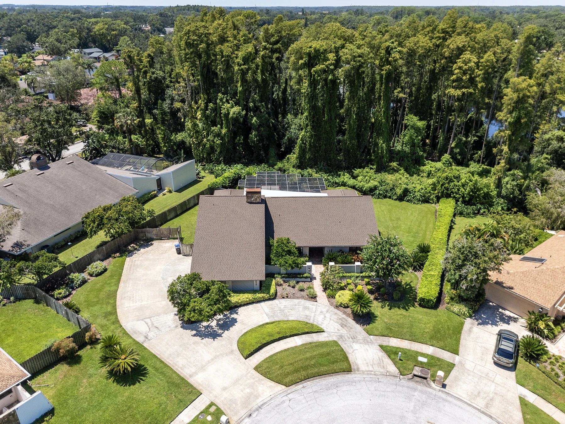 Aerial view of a Carrollwood Village home in Tampa with a circular driveway, pool enclosure and conservation backdrop