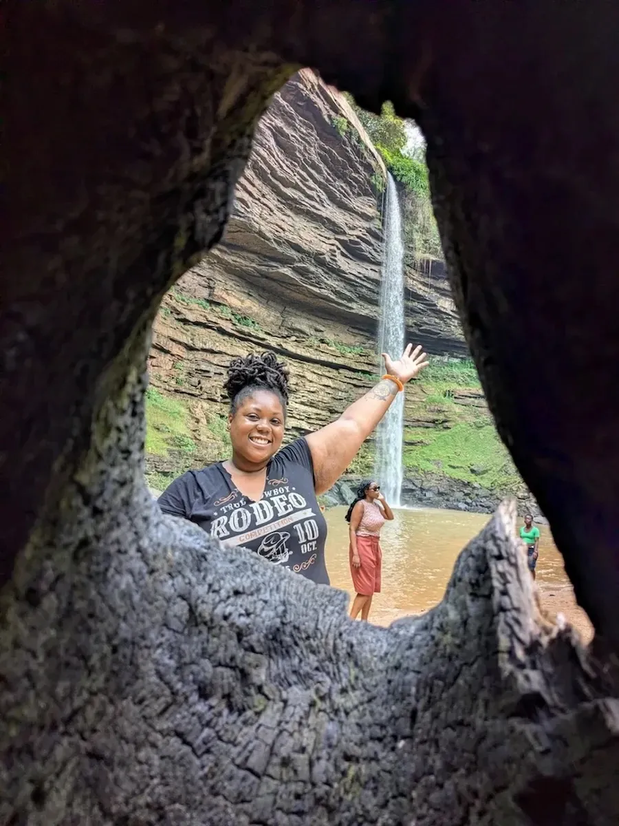A group of happy travelers posing for a photo at the base of Boti Falls on a BookAfrica Nature Adventure.