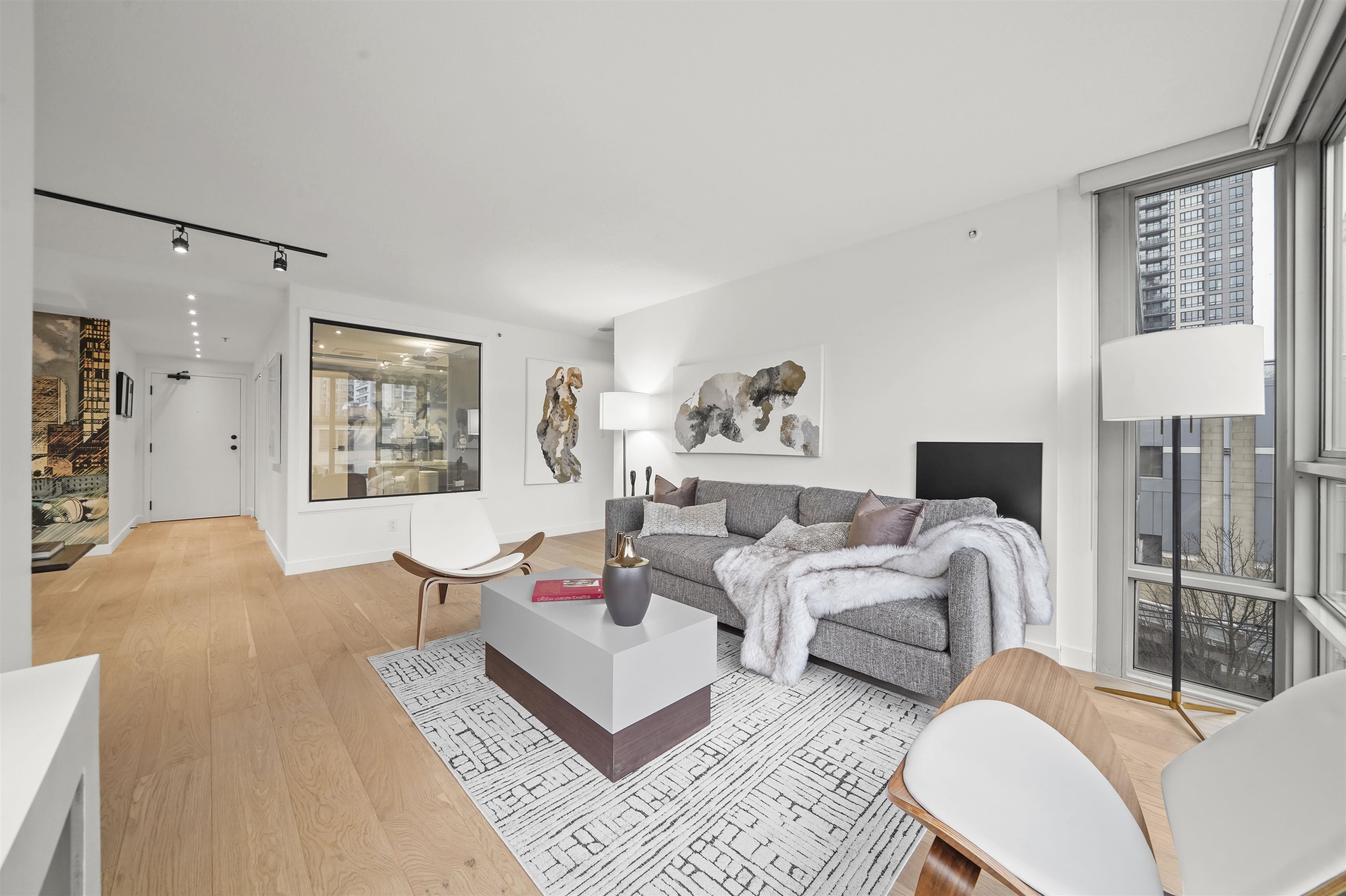 Modern living room with light walls, contemporary furniture, and large windows providing natural light.