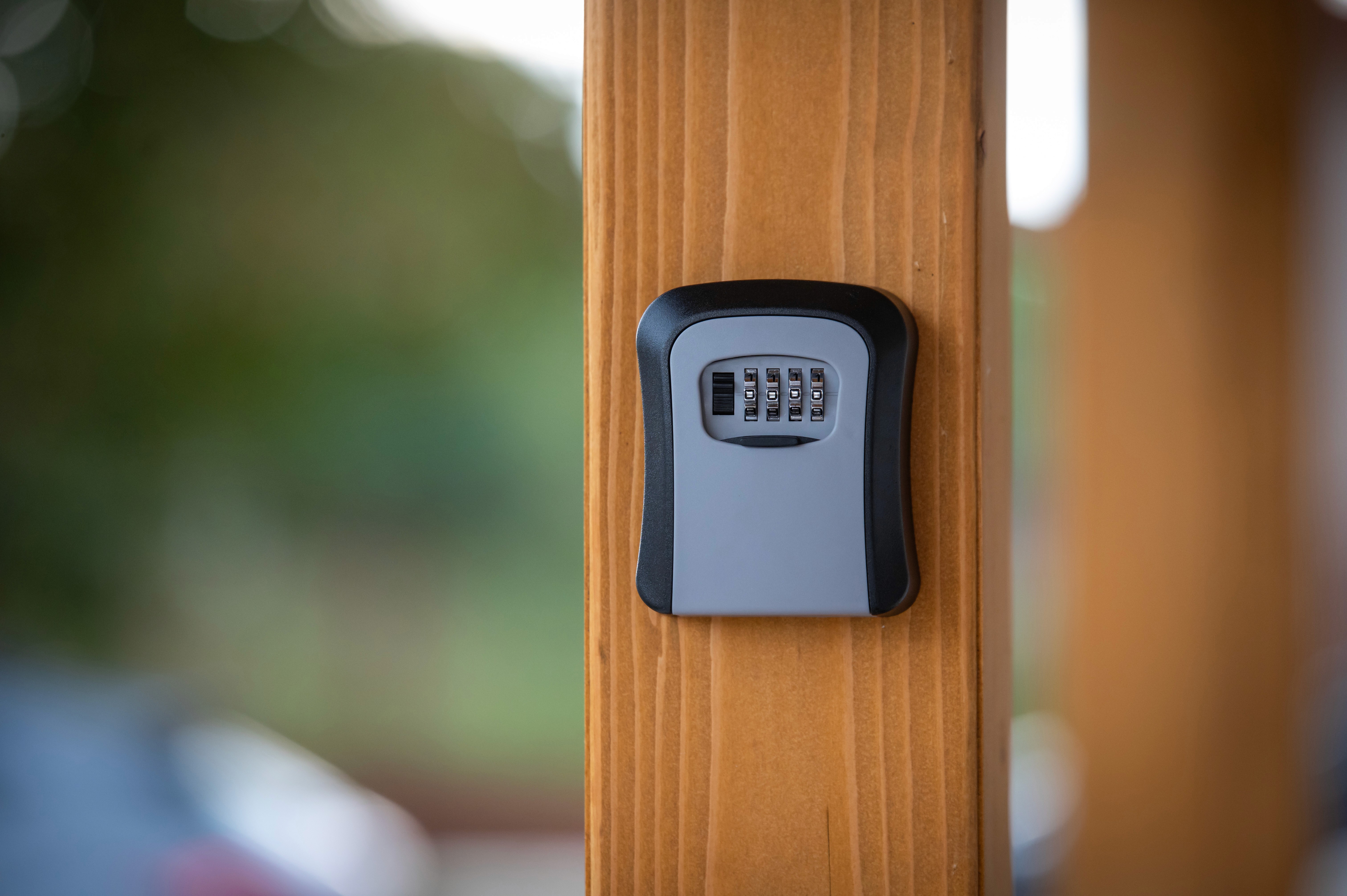 Szürke kombinációs kulcsszéf faoszlopra rögzítve kültéri környezetben.