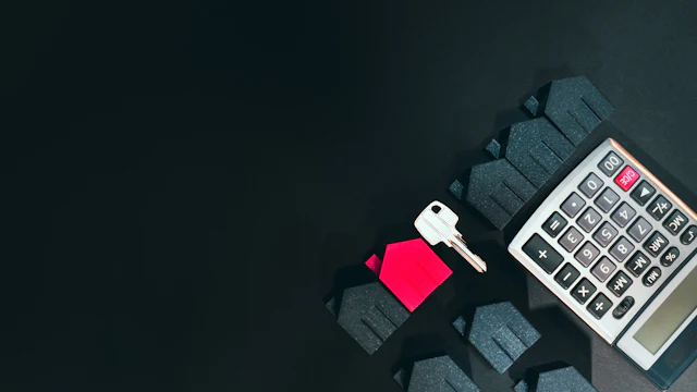 A silver key, a red house model, and a calculator on a black surface