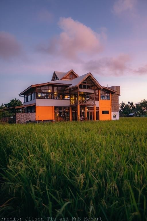 A modern two-story building with orange accents standing in a vast green field under a twilight sky.