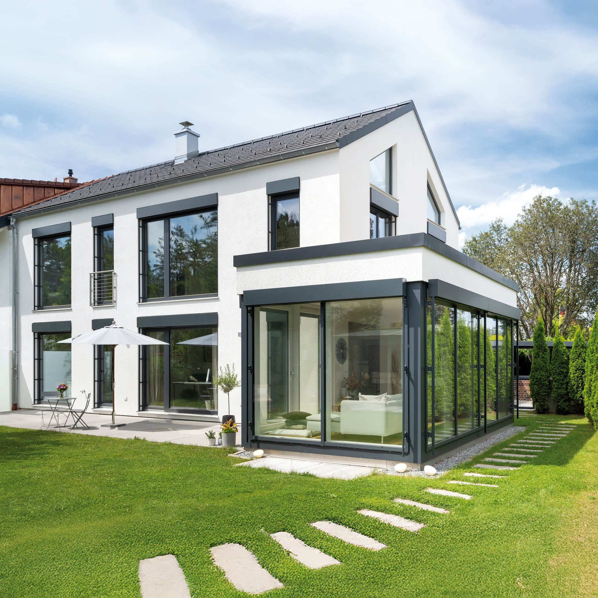 Modernes, weißes Einfamilienhaus mit großflächigen Fensterfronten, einem Wintergarten und gepflegtem Garten.