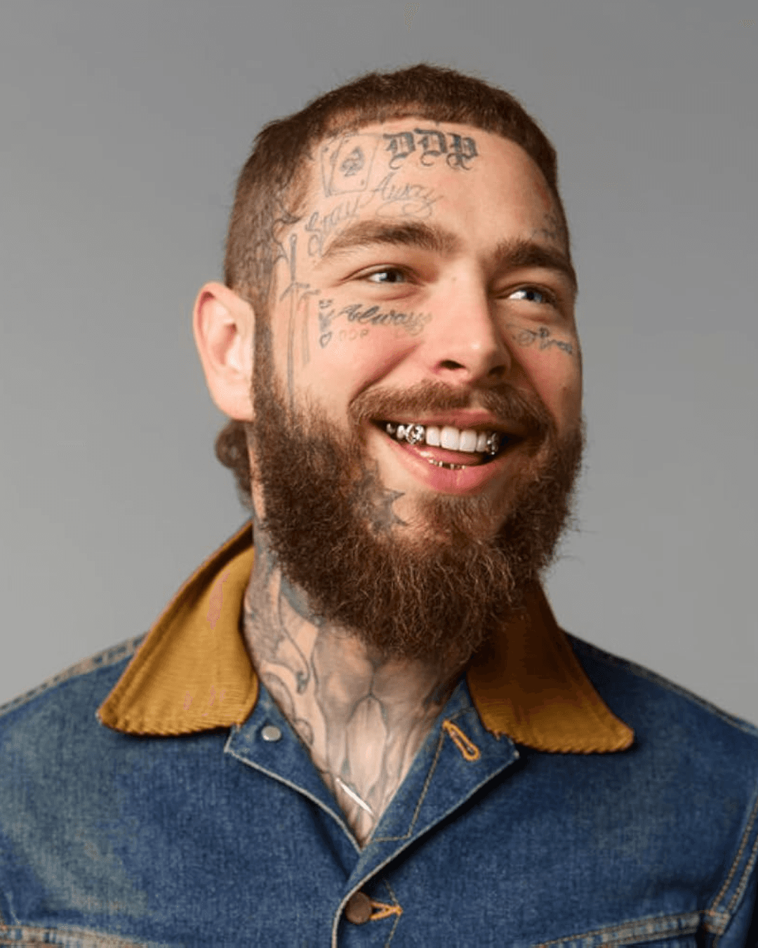 Post Malone, a smiling man with a beard and tattoos, wearing a denim jacket, posed against a neutral background.