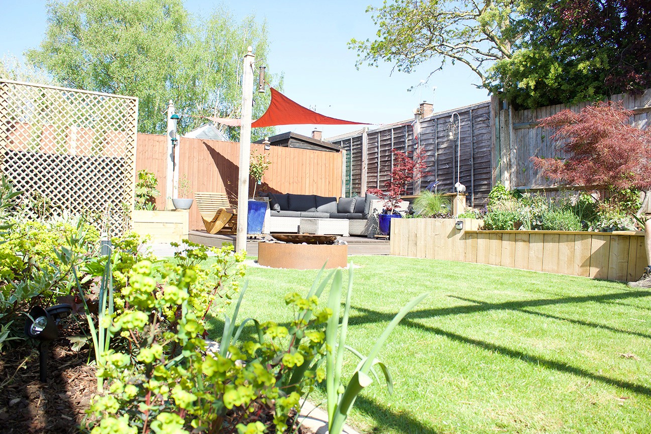 A sunny garden with green grass, colorful plants, and a wooden structure in the background.
