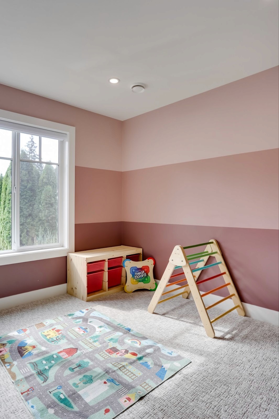 Playful children’s room with ombre pink striped walls and grey carpet.