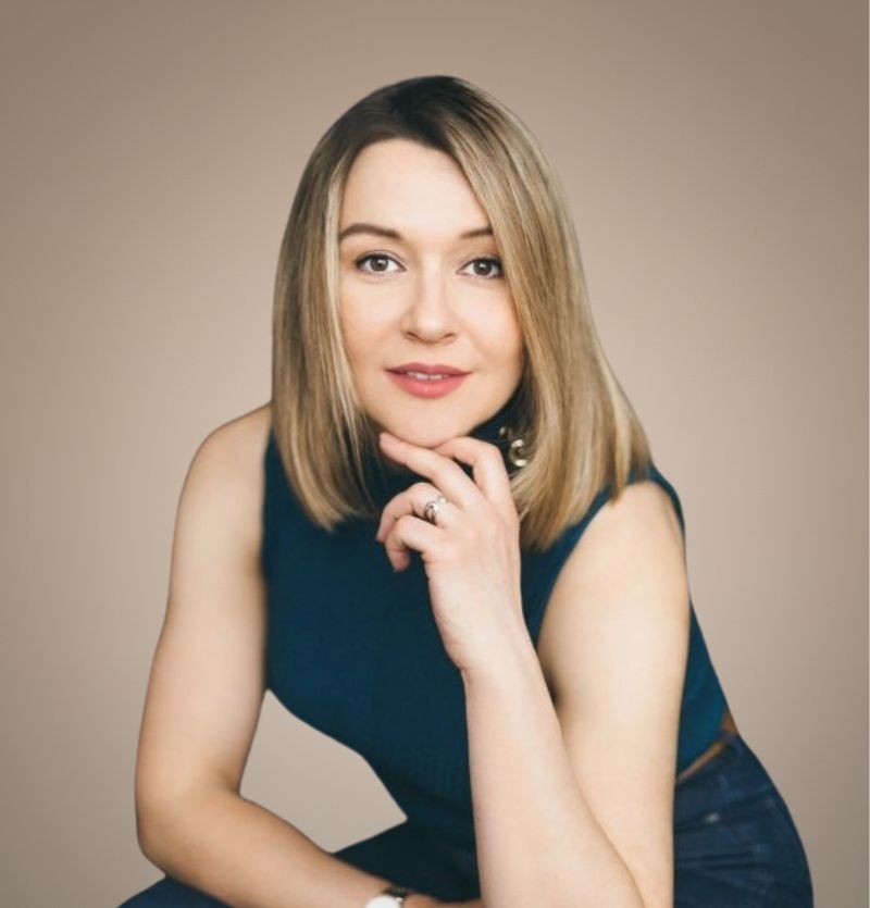 A confident person with short, styled hair and a leather jacket poses against a dark backdrop.