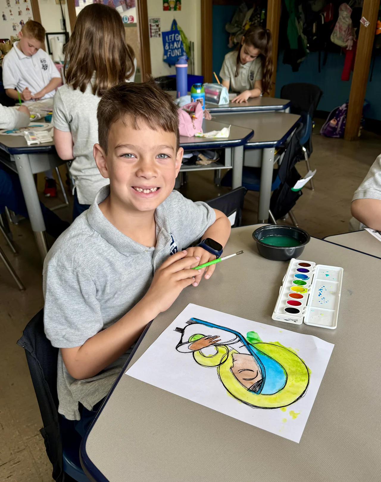 A student smiling at his desk with the watercolor painting he made