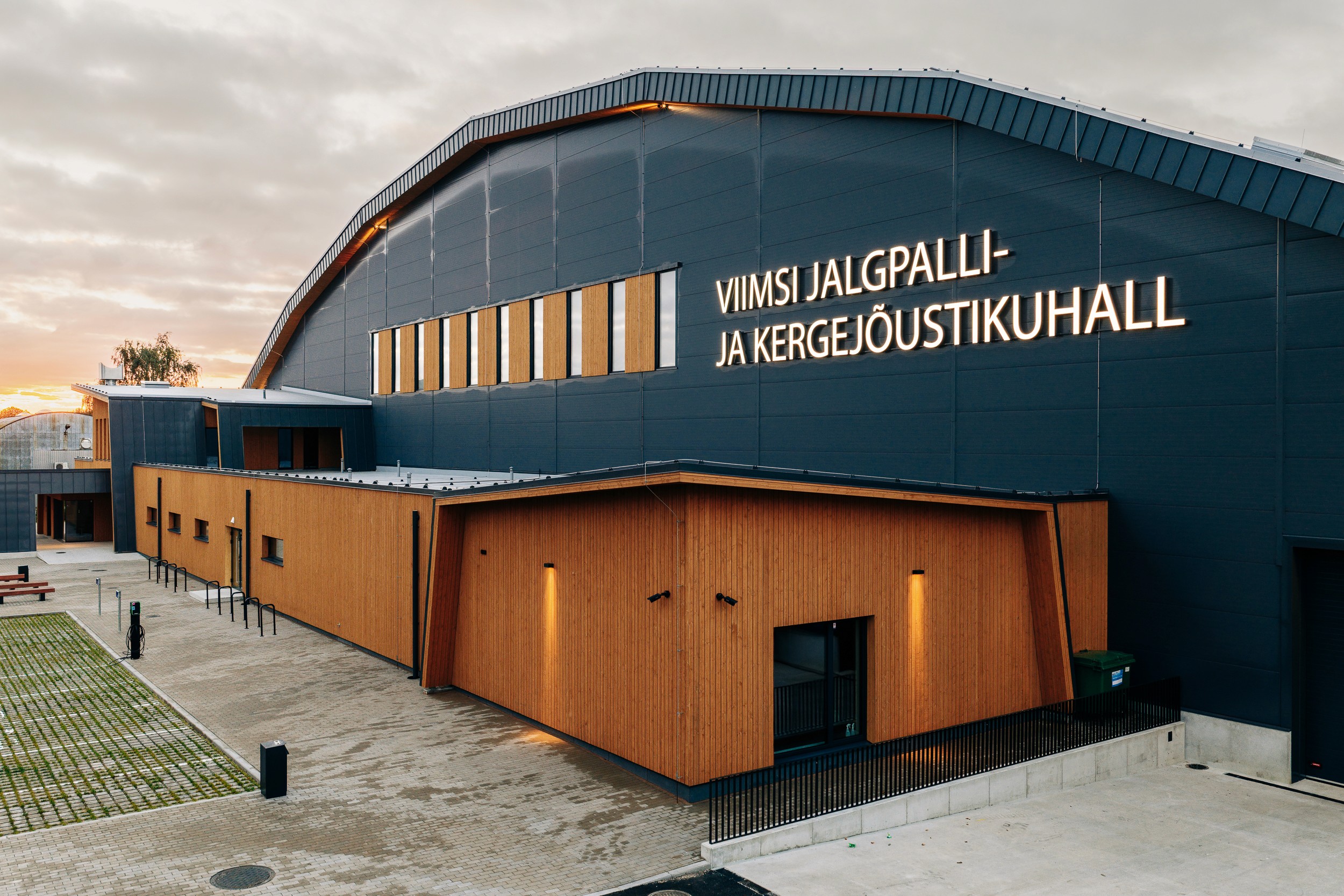 Exterior view of the Viimsi sports hall showing its timber-clad entrance volume and signed facade.
