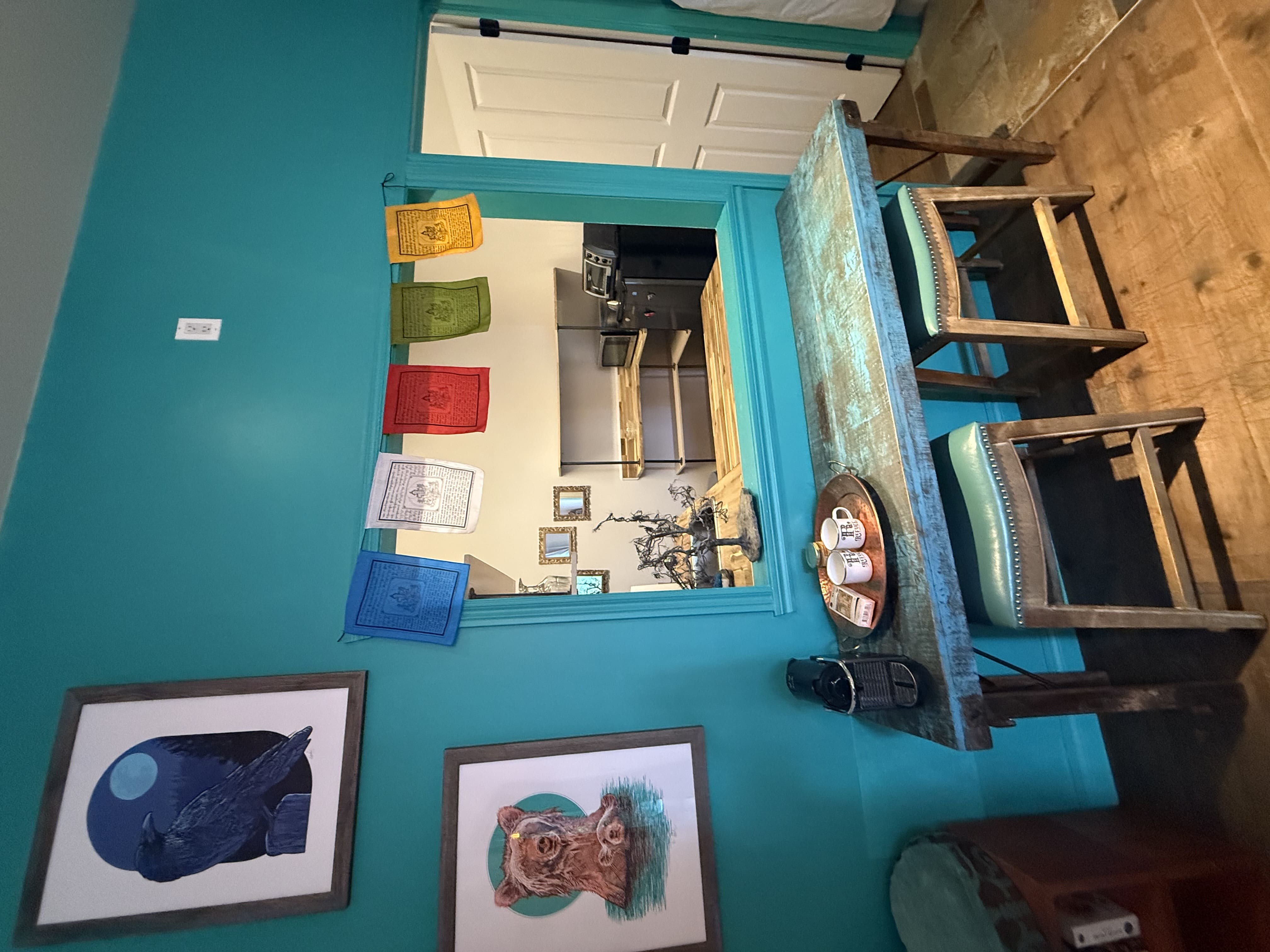 Mur turquoise décoré de drapeaux de prières tibétains, table rustique en bois avec machine à café et tasses.