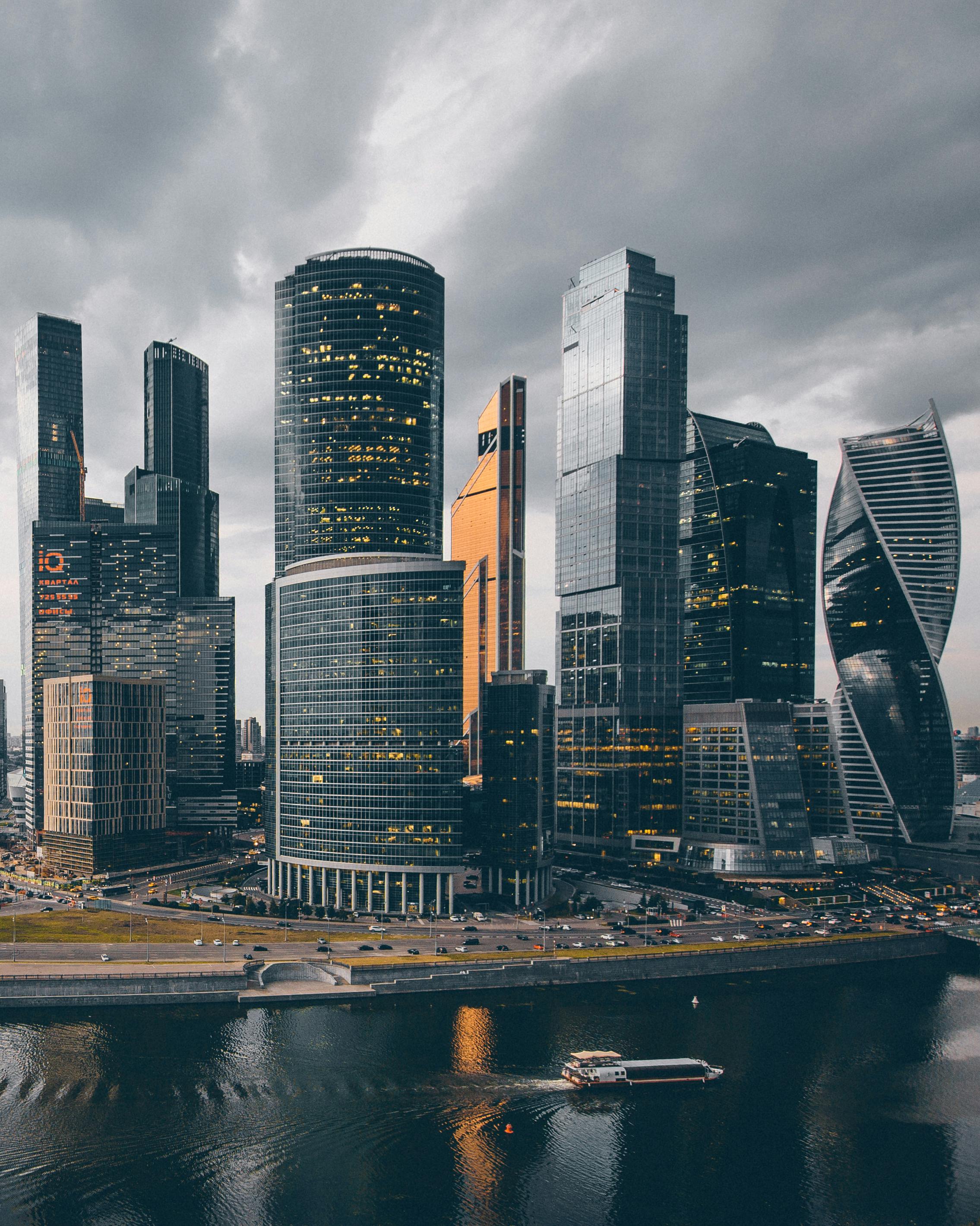 Modern skyline of a financial district with high-rise office towers beside a river under cloudy skies.