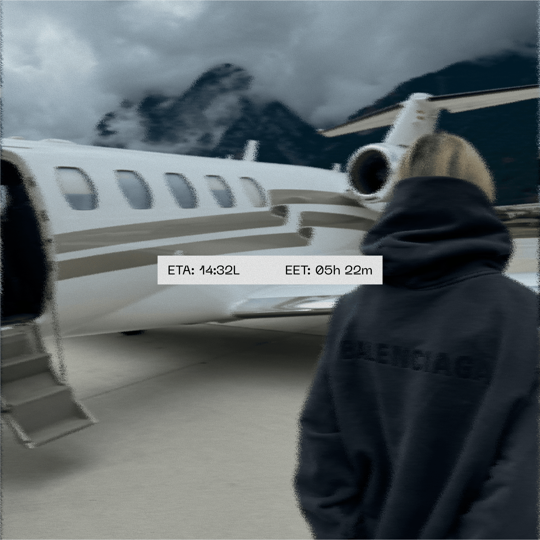 A person in a dark hoodie stands beside a private jet on an overcast day, with misty mountains in the background.