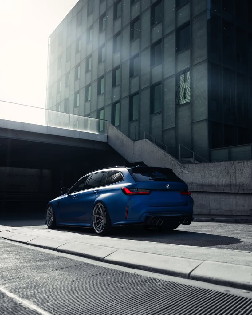 BMW M3 Touring bleue mate garée devant un bâtiment moderne