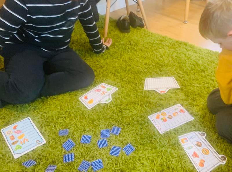 A Horizon Hub team member and a child are playing a game on the carpet. It's a shopping list card game.