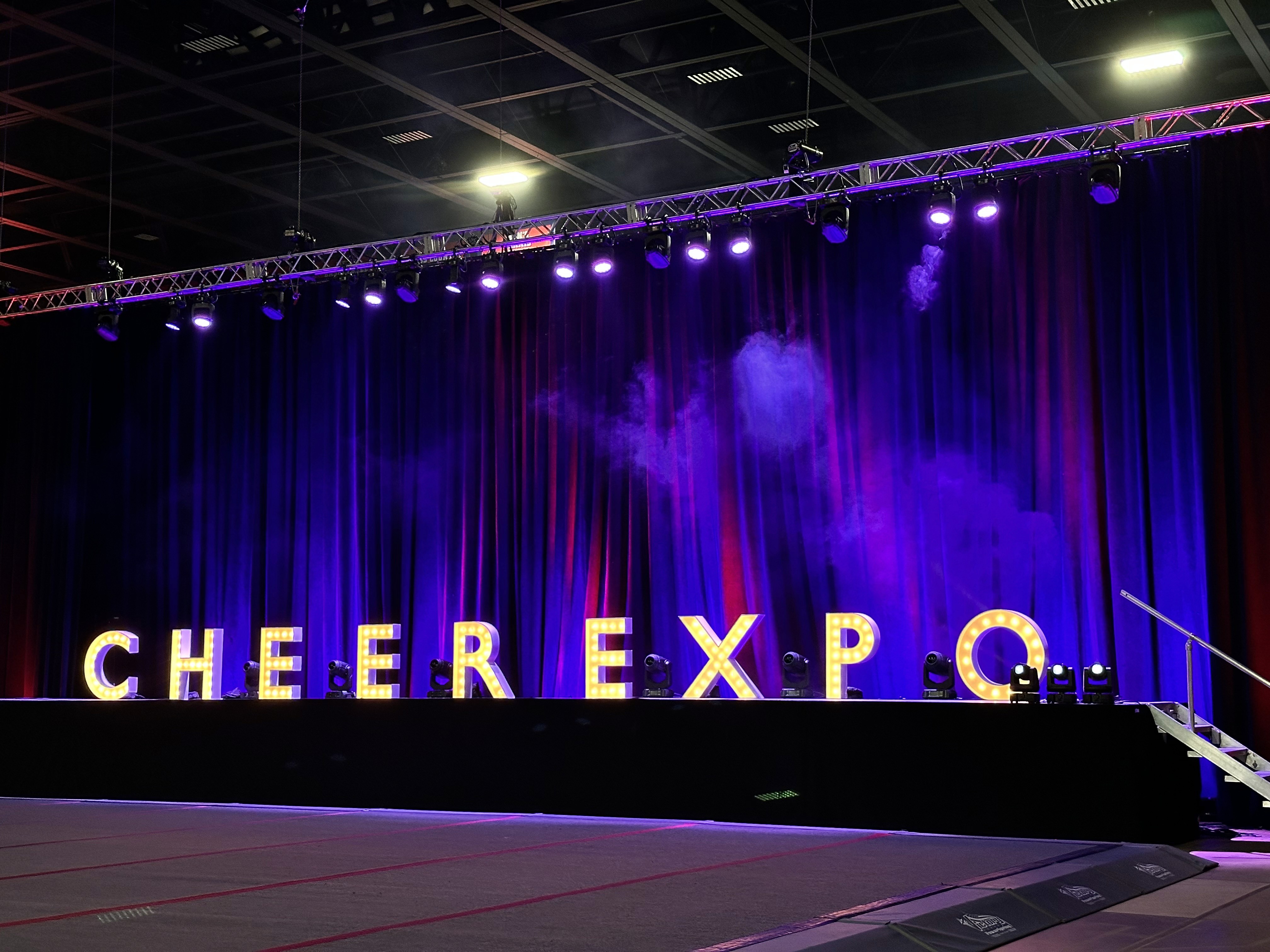 Indoor arena with purple stage lighting and Cheer Expo branding