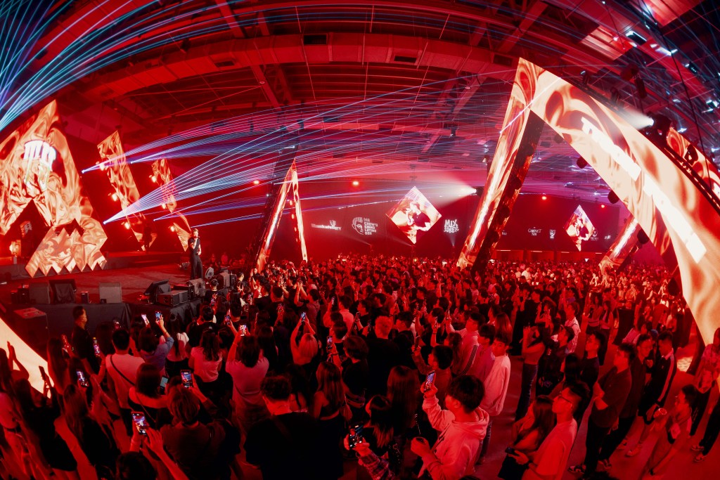 A vibrant crowd at a live music event with dynamic lighting and a performer on stage, showcasing a lively atmosphere.