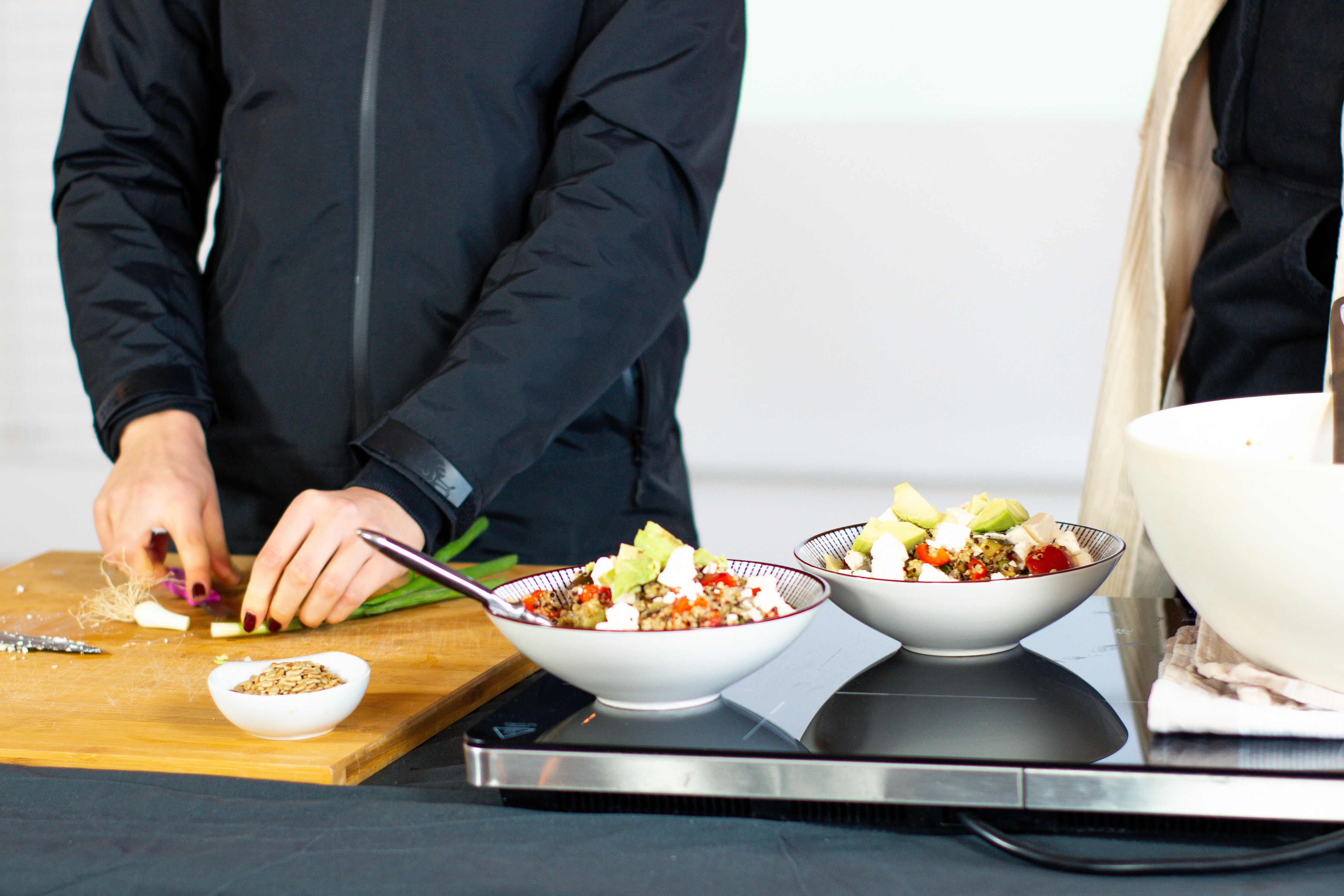 Zwei Schalen mit vorbereitetem Essen mit Obst, daneben eine Frau, die Lauch schneidet