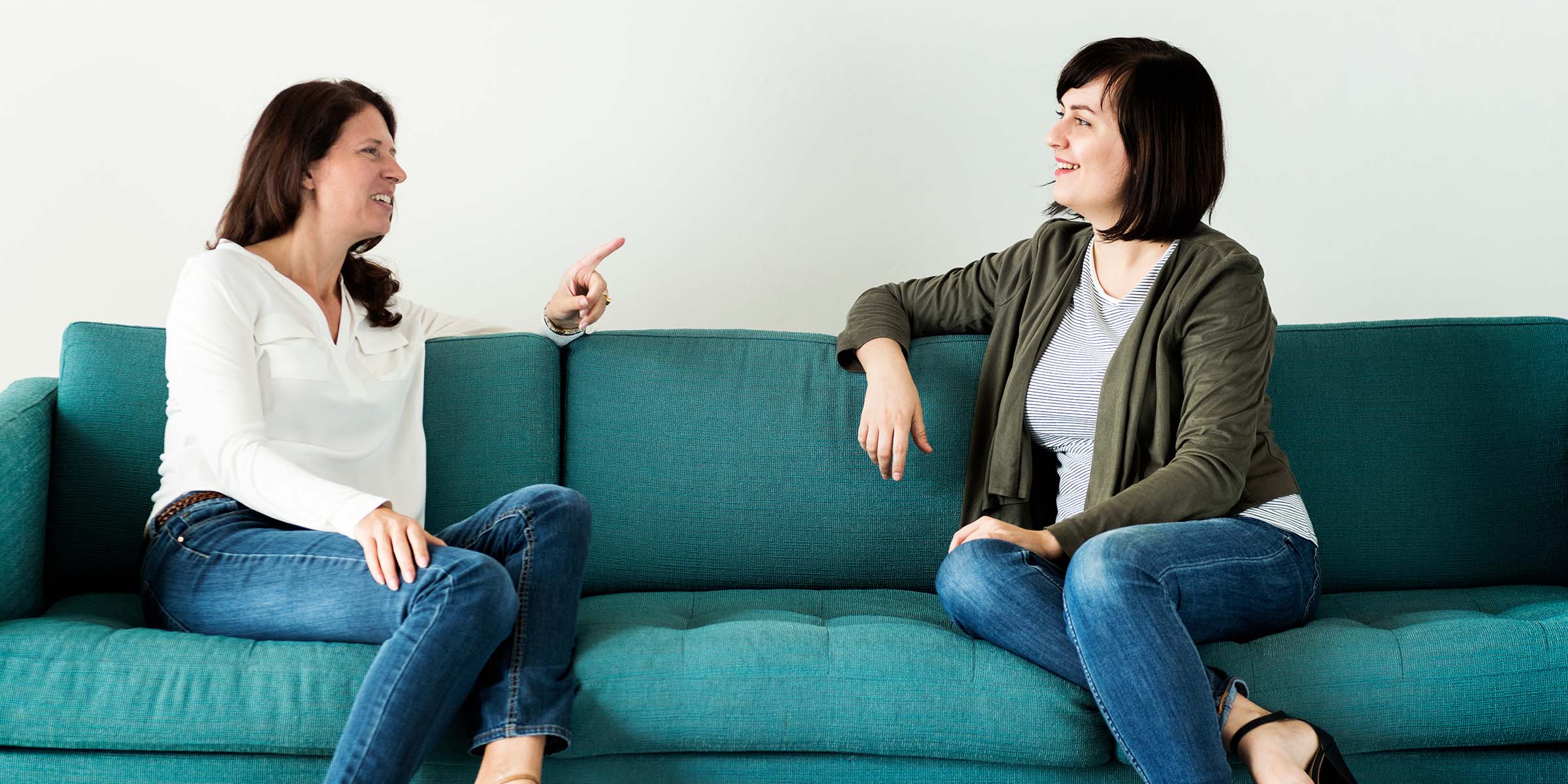 Two women sat on a sofa having a happy converstation