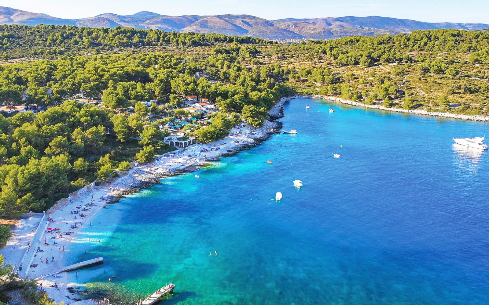 Aerial view of Duga Bay with turquoise waters, boats, and a forested coastline.