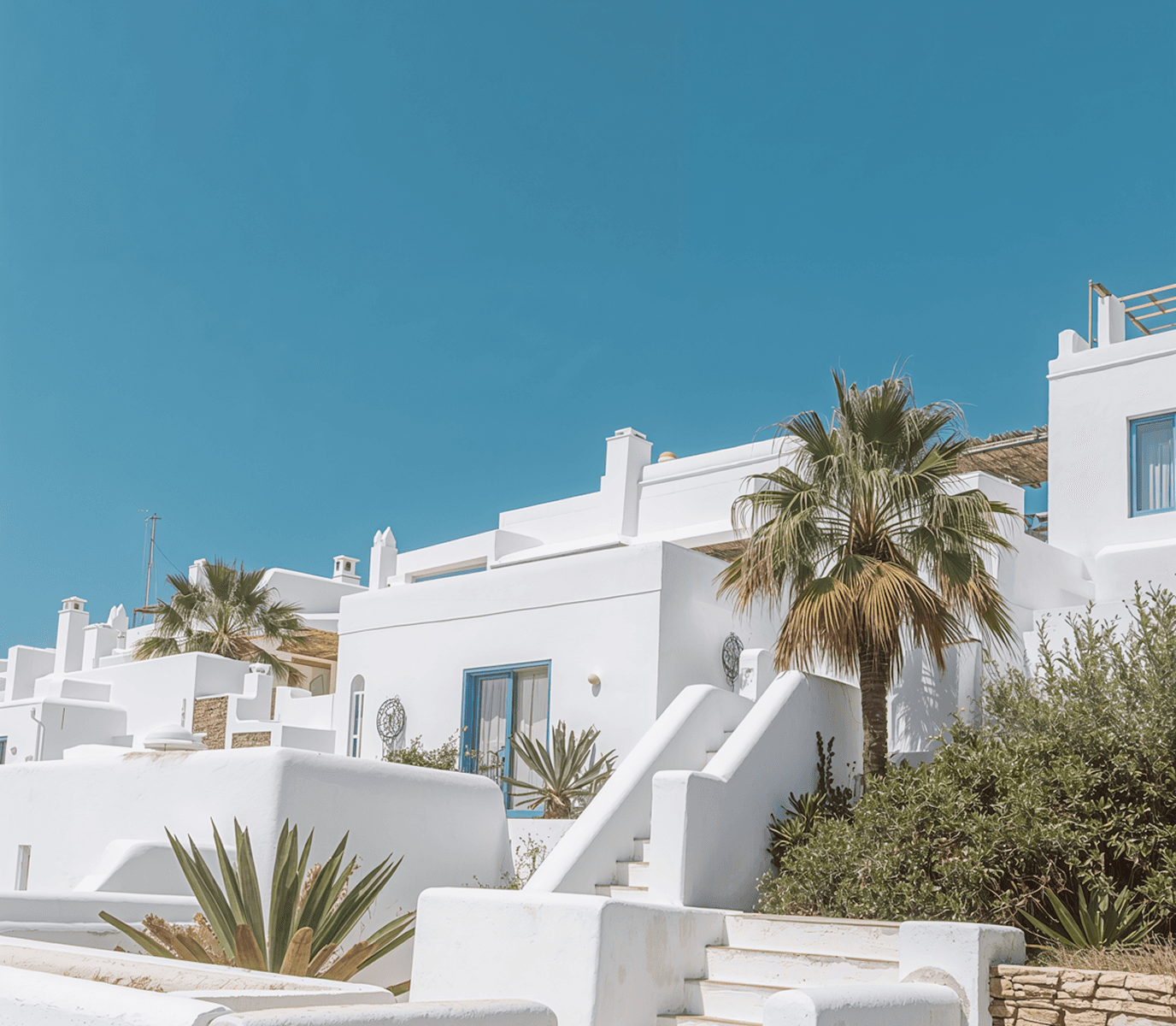 White Mediterranean style houses with palm trees under clear blue sky