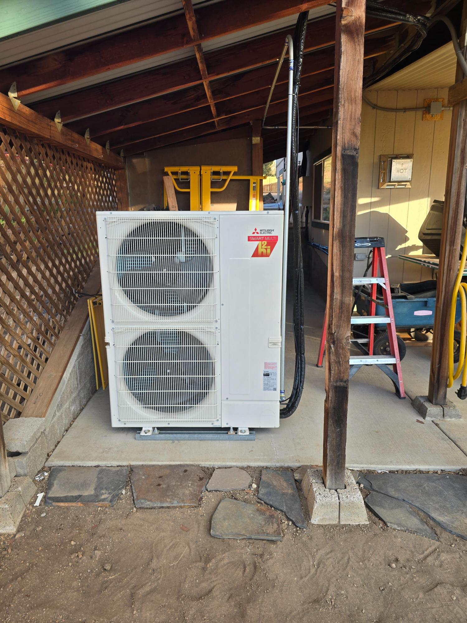 Outdoor Mitsubishi heat pump system installed under a patio cover.