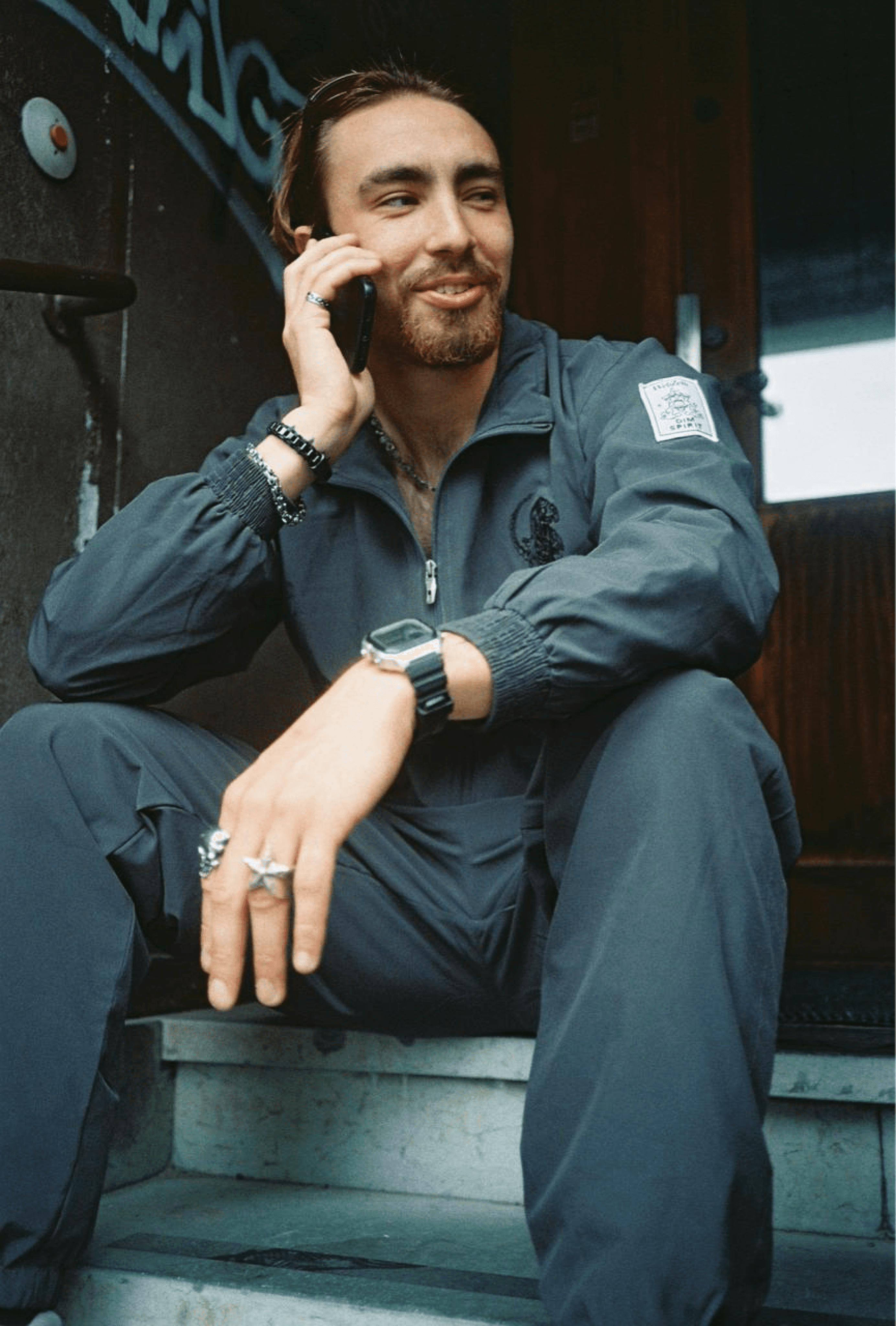 Model wearing the Dim Spirit x WebZero windbreaker tracksuit, seated on steps