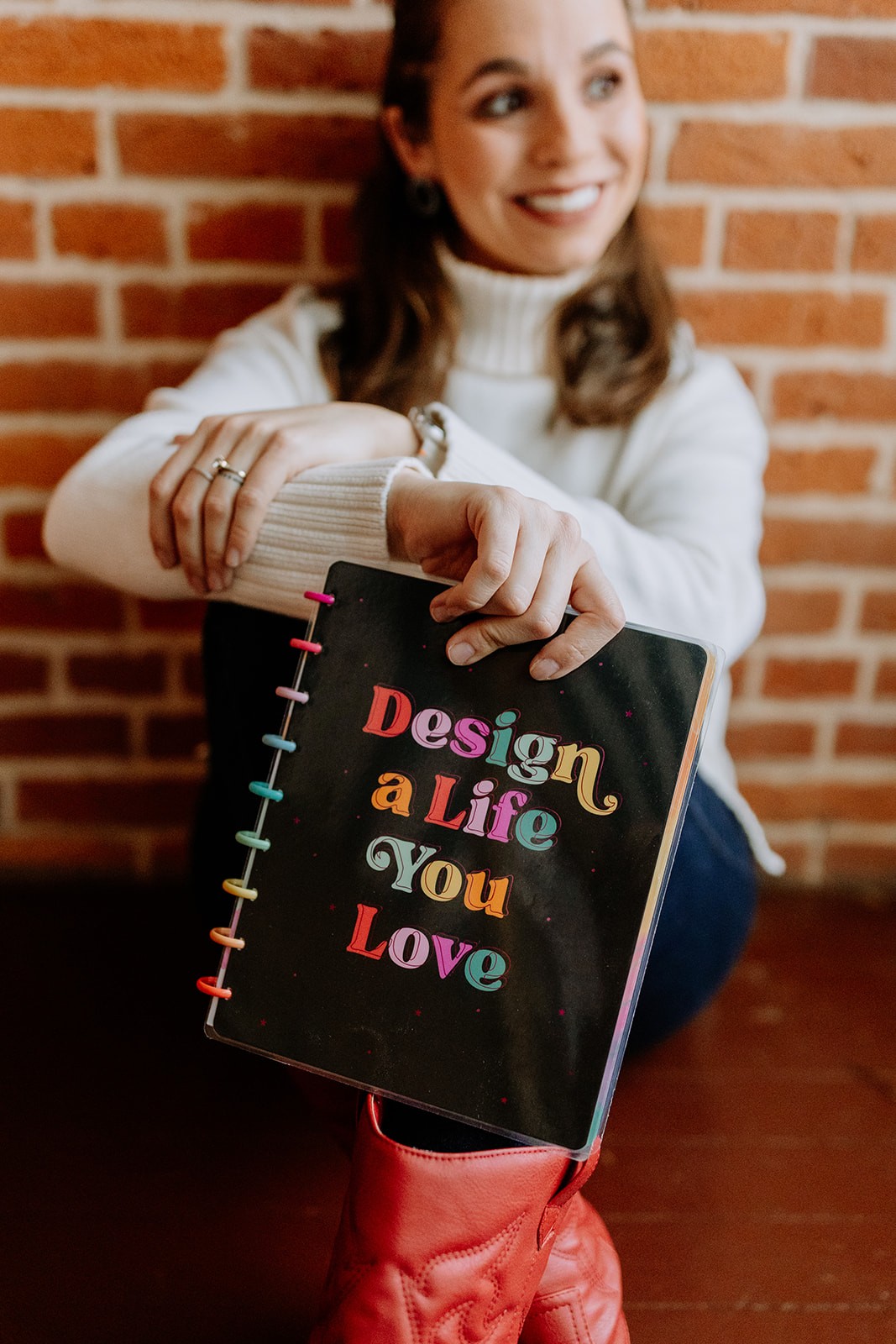 Founder and Designer Jamille Ramos smilling and holding a notebook that says "Design a Life You Love".
