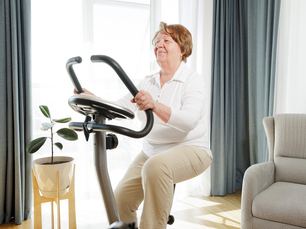 older woman using a stationary bike to do low-impact cardio exercise to lose weight at home in her living room
