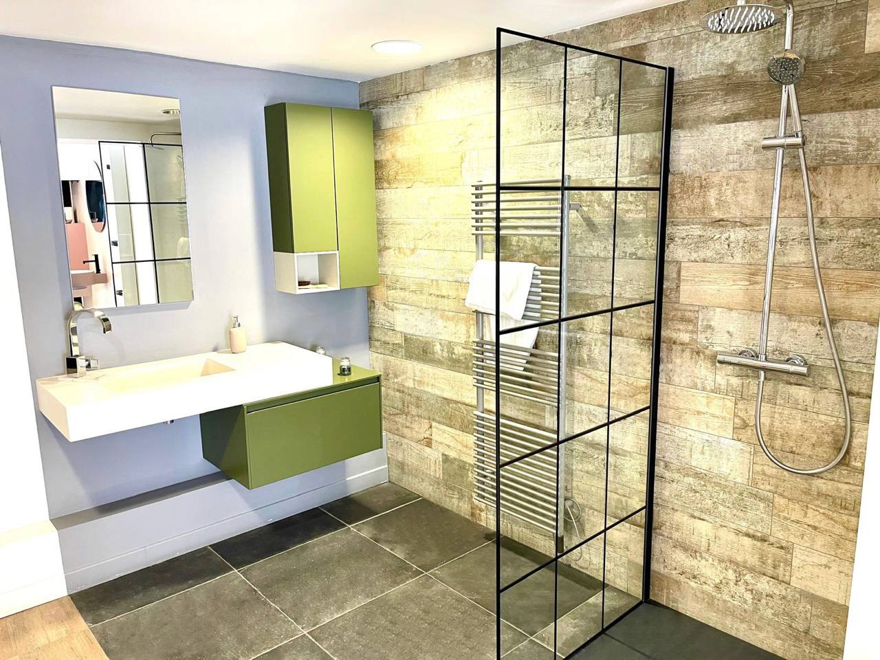 Salle de bains exposition Seine-et-Marne avec meubles flottants verts, douche italienne et carrelage effet bois, showroom.