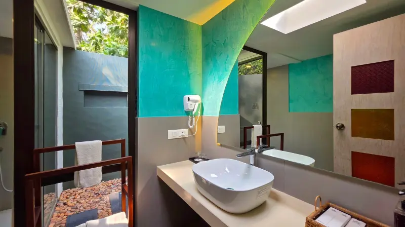 Lake View Villa bathroom at Vedic Village Kodungallur with teal accent wall, oval vessel sink and glass-walled outdoor shower with pebbled flooring