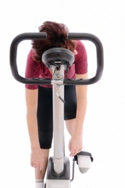 a tired woman leaning on a spin bike