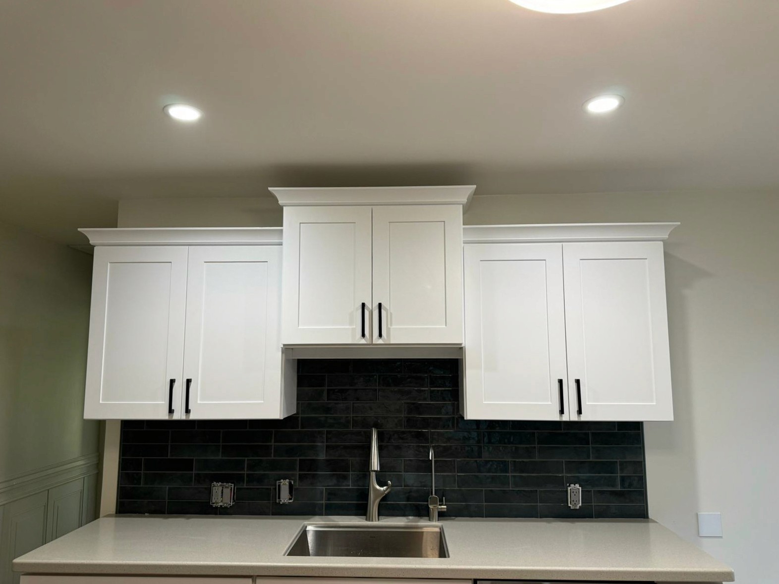Contemporary kitchen with white cabinets, a black subway tile backsplash, and a stainless steel sink under recessed lighting.