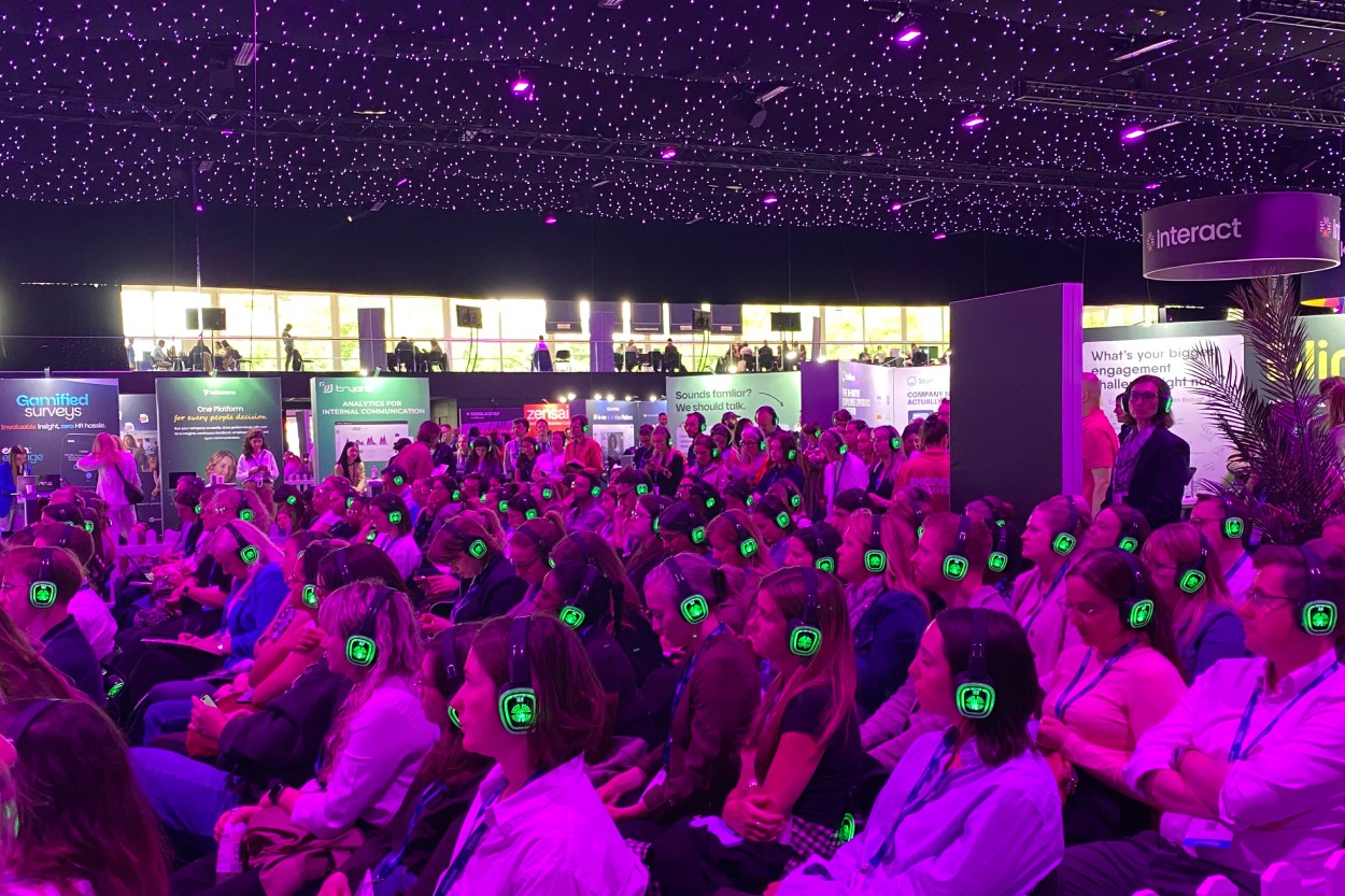 Packed conference hall at Engage Employee Summit, with hundreds of attendees wearing glowing green headphones under purple lighting.Packed conference hall at Engage Employee Summit, with hundreds of attendees wearing glowing green headphones under purple lighting.