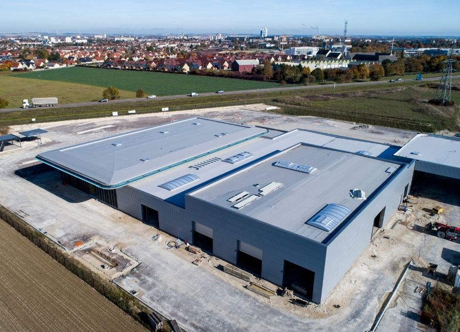 Vue aérienne d’un bâtiment industriel avec toiture plate, situé dans une zone en développement.
