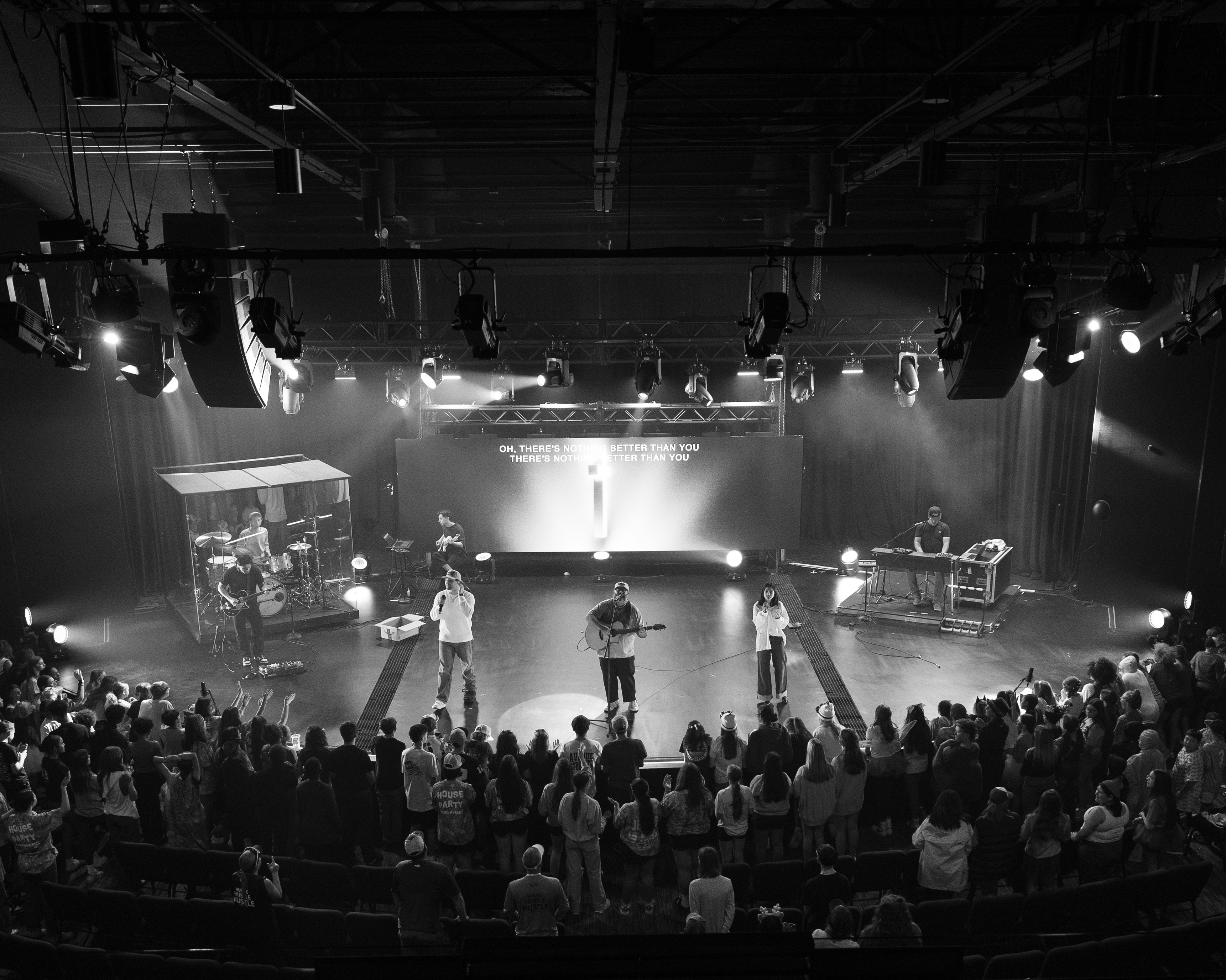 A speaker stands on stage in front of an audience, presenting with a projector screen behind them.