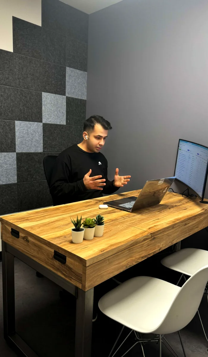 Close-up portrait of a person wearing a gray insulated hooded jacket with the hood up, showing their face framed by the hood against a light background.