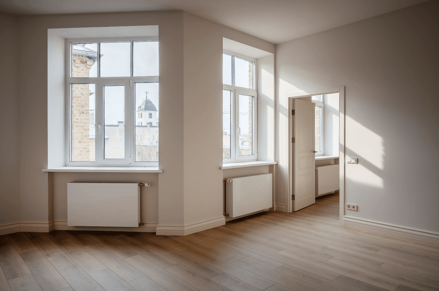Row of modern white villas with balconies, surrounded by green grass under a clear blue sky.