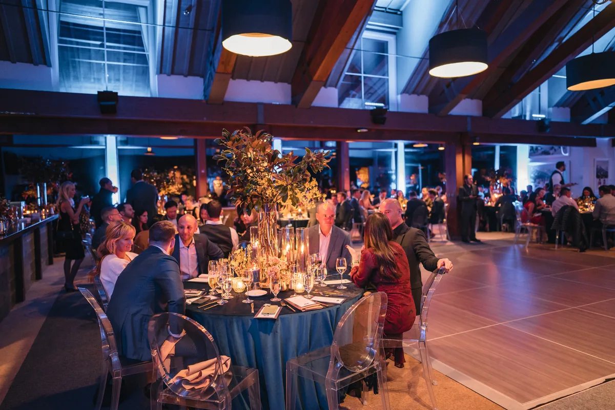 Woodline Partners guests sit around candlelit dinner tables beneath the Sundeck’s timber ceiling and blue event lighting.