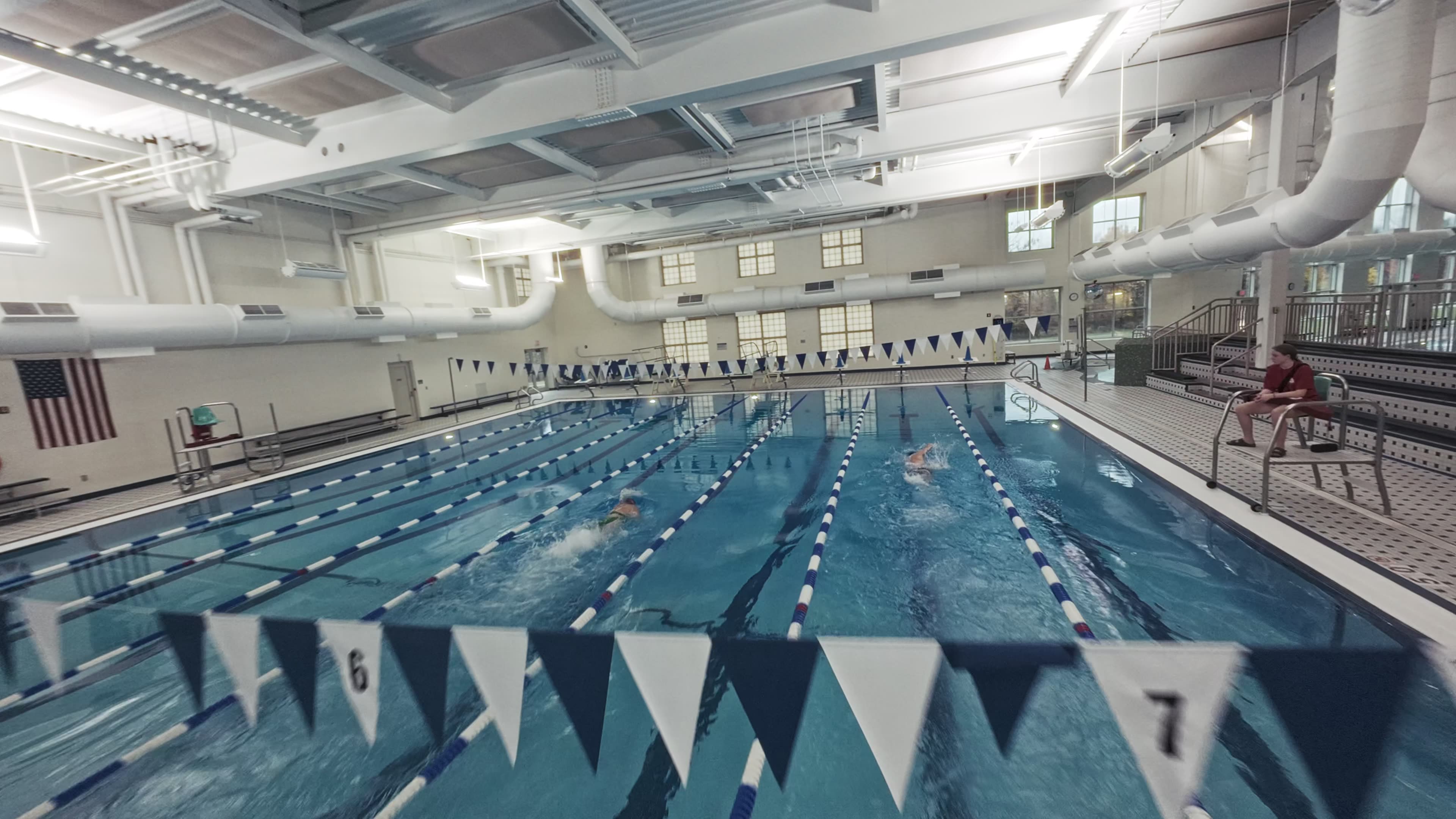 Modern glass and wood cabin with a cozy outdoor deck featuring wicker furniture, surrounded by lush green trees and a serene forest setting.