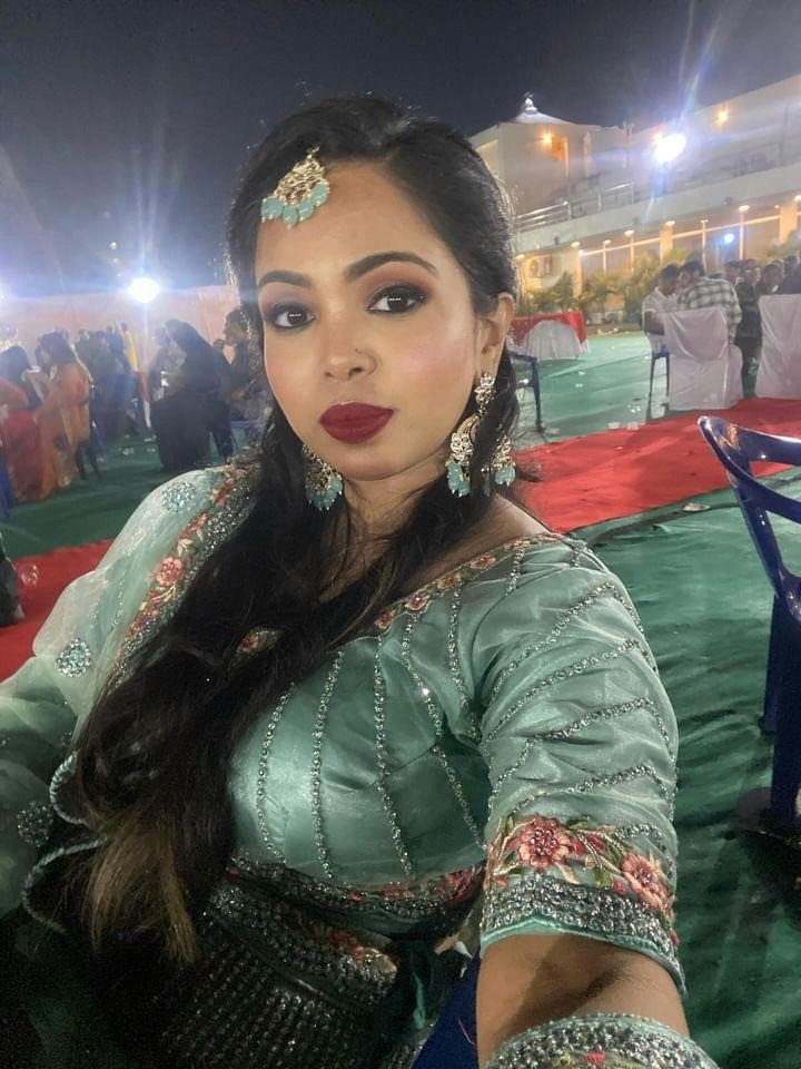 A smiling young man with crossed arms, wearing a plaid shirt and white t-shirt, poses against a dark background.