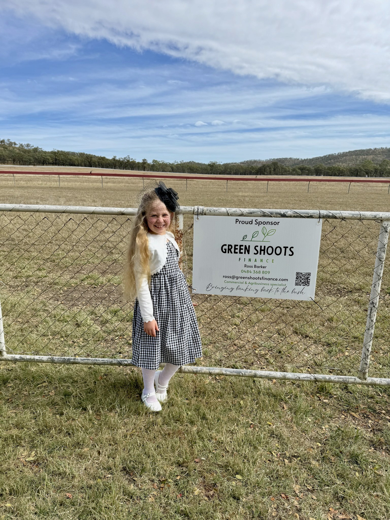 Ross's daughter at a Green Shoots Finance sponsorship sign during local horse races, showing community support