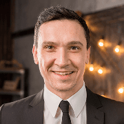 Smiling middle-aged man in a dark professional suit and white shirt, featuring a warm and approachable expression.