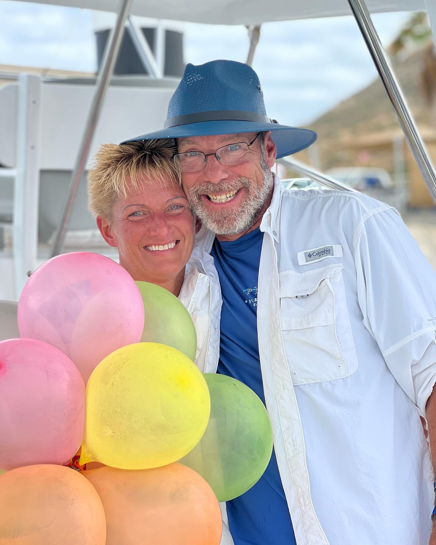 Two people smiling and posing together holding colorful balloons at an outdoor event by Be Bold Balloons