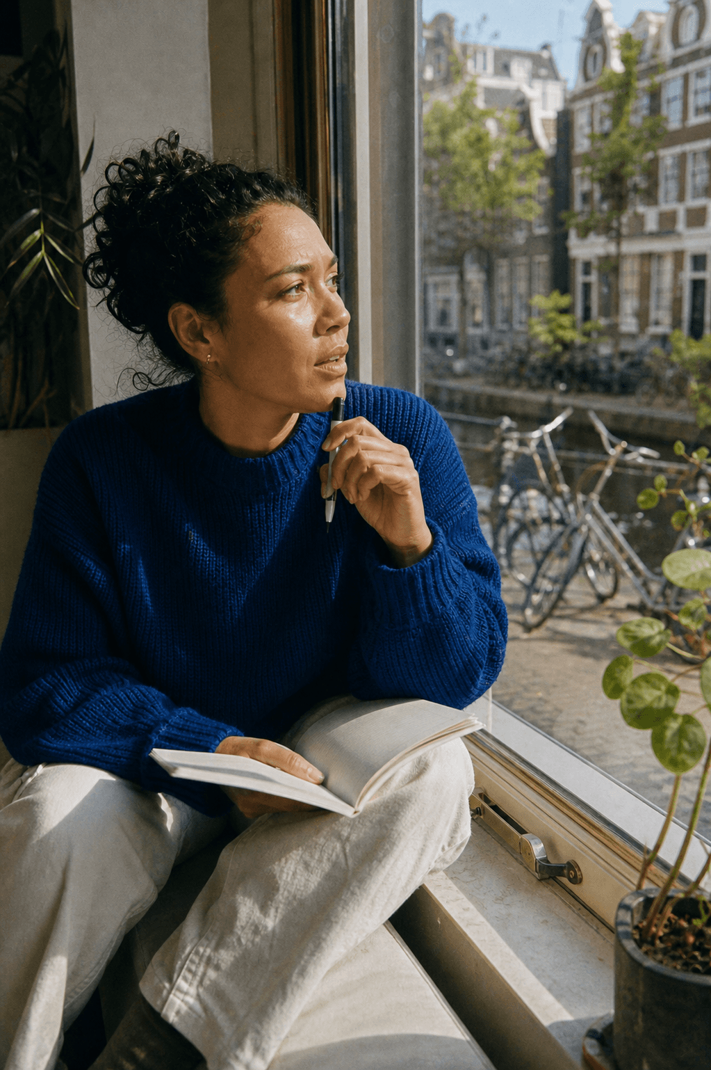 Pausing over a paper notebook on a canal-side office windowsill as a question occurs to her.