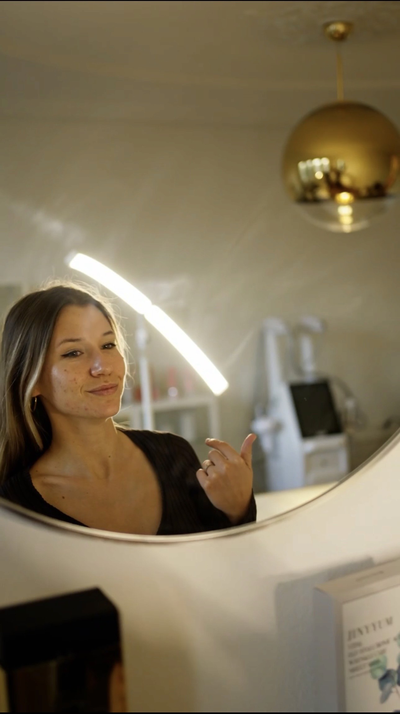 Woman in a towel and head wrap applying skincare cream in a cozy bedroom