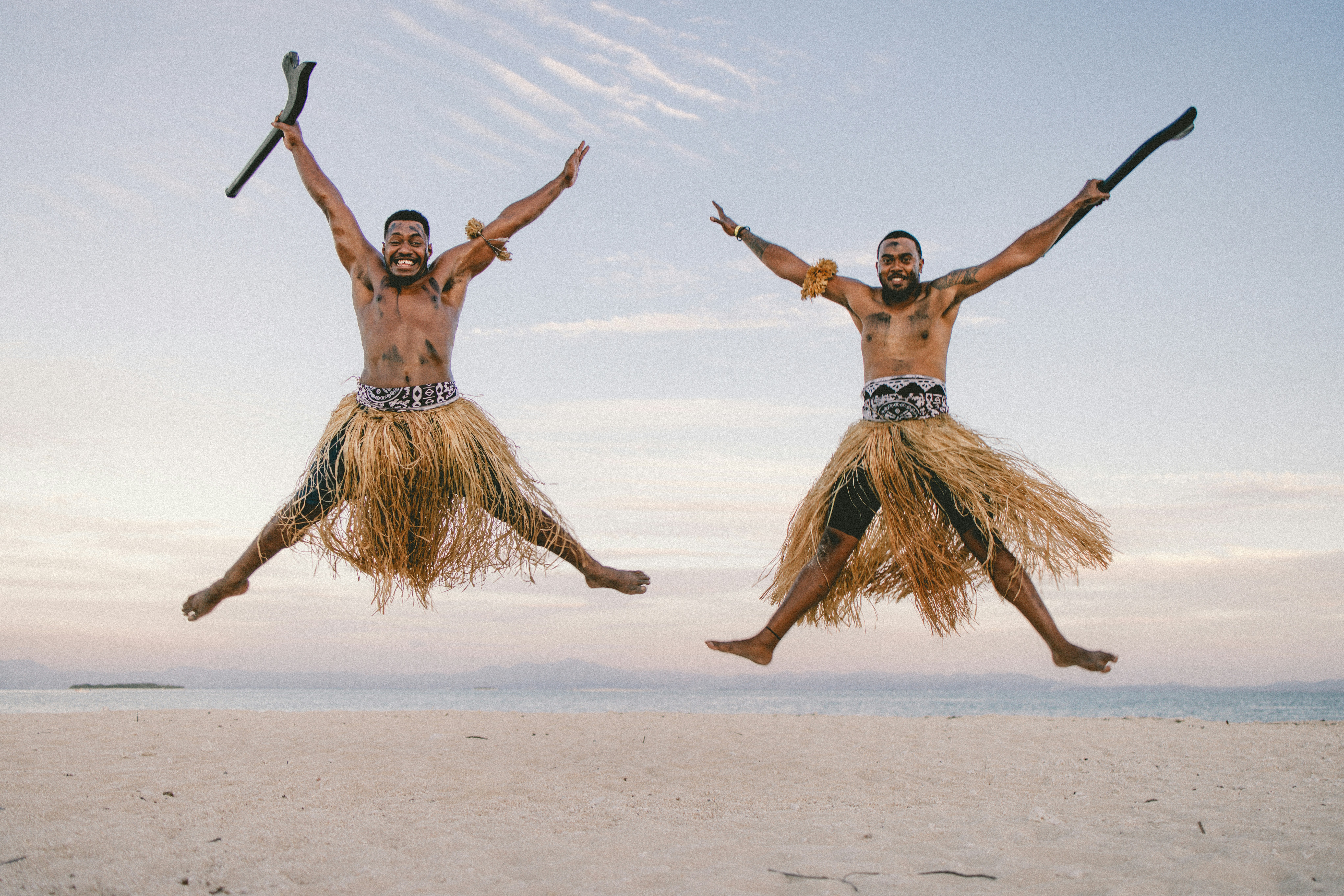 two men in grass skirts jumping in the air