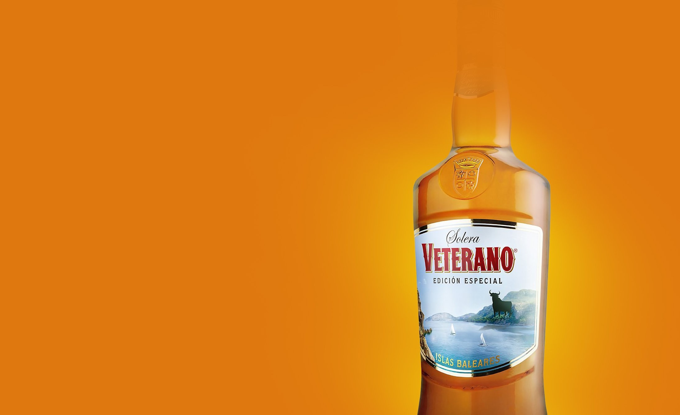 A bottle of Veterano Brandy, "Edición Especial," is set against a vibrant orange background. The label features a black bull silhouette and ocean scene.